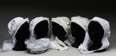 trois mannequins noirs coiffés de bonnets blancs et vêtus de tissu blanc