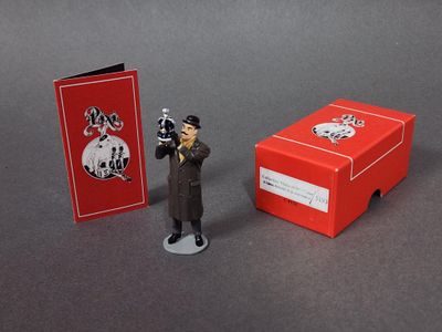une petite figurine représentant un homme tenant un pistolet à côté d'une boîte rouge
