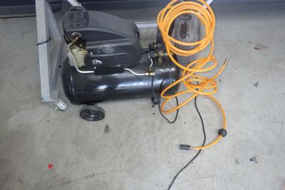 un petit compresseur d'air posé par terre, auquel est raccordé un tuyau