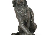 bronze statue of a dog sitting on a rock on a white background