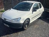 La voiture blanche est garée sur le parking, à côté d'une clôture.