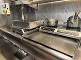 un plan de travail en acier inoxydable sur lequel sont posés des casseroles et des poêles, dans une cuisine professionnelle