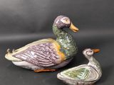 deux canards en céramique assis l'un à côté de l'autre sur une surface noire