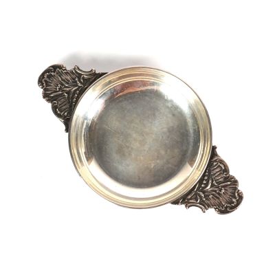 une assiette en argent avec une poignée, posée sur un fond blanc