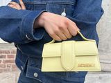 woman in denim jacket and jeans holding a yellow purse in front of a brick building
