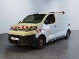 La camionnette blanche est garée dans une grande pièce ; elle porte une bande rouge et blanche sur le côté.