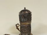 une petite cafetière en argent avec une anse, posée sur une surface blanche