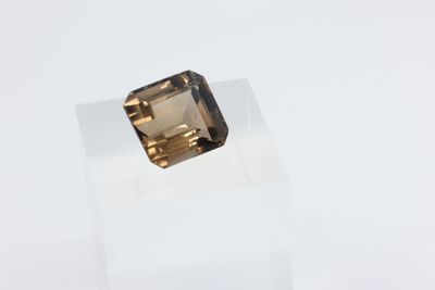 un gros plan d'une pierre de quartz fumé taillée en carré, posée sur un socle en acrylique transparent