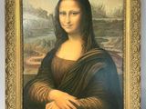 painting of a woman ' s face in a gold frame on a white wall