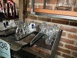 bottles and glasses are lined up on a table in front of a brick wall