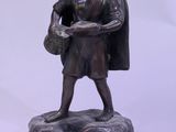 une statue représentant un homme tenant un panier, assis sur un rocher
