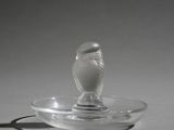 a small glass bird sitting on top of a glass plate