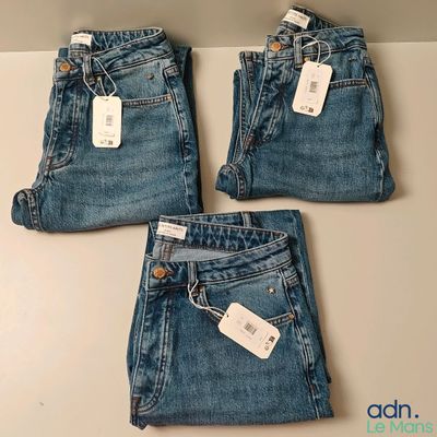 trois paires de jeans, encore étiquetées, posées sur une table