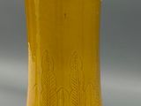 a yellow vase sitting on a table with a gray background