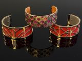 two red and gold cuff bracelets sitting on top of a black surface