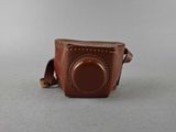 brown leather camera case with a small lens on a gray surface