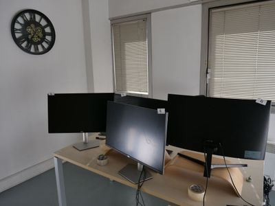 trois écrans d'ordinateur posés sur un bureau, avec une horloge en arrière-plan