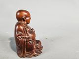 a small wooden statue of a monk sitting on a white surface