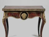 une petite table dont le plateau est orné de motifs dorés et rouges