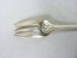 a silver fork with a flower on it on a white surface