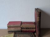 Plusieurs vieux livres sont empilés sur une table, avec un mur blanc en arrière-plan.