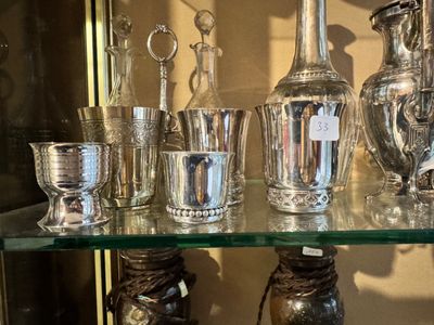 a glass shelf with silver vases and silver cups on it