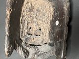 a wooden mask hanging on the wall with a tag on it