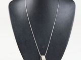 silver necklace with a rectangle shaped pendant on a black mannequin
