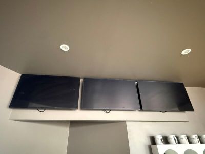 three televisions mounted on the wall above a stove