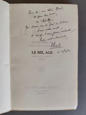 un livre ouvert, sur lequel est inscrit un poème manuscrit, posé sur une table