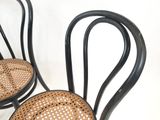 une paire de chaises en métal noir avec des assises en osier, posées contre un mur blanc