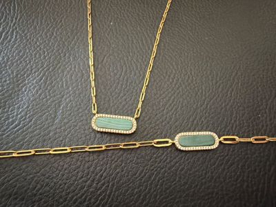 two gold and green necklaces on a black leather surface