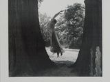 photographie en noir et blanc d'une femme debout devant un arbre
