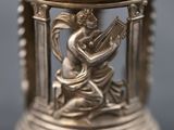 a close up of a silver vase with a woman playing a musical instrument