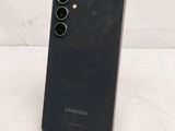 a close up of a black samsung phone on a white surface