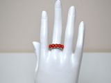 a white hand with a red beaded ring on it