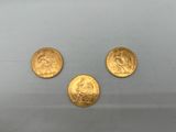 On voit trois pièces d'or sur une surface blanche