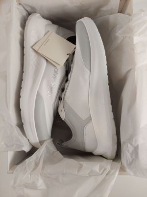des baskets blanches dans une boîte, avec une étiquette posée dessus