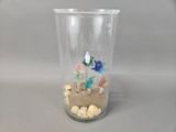 a glass vase with a sand and shells inside of it