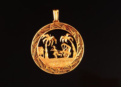 une image représentant un pendentif en or orné d'un bateau et de palmiers