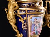 a blue vase with a painting on it next to a gold candelier