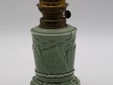 un petit vase vert avec un couvercle doré, posé sur une surface blanche