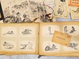an open book sitting on top of a bed next to a bunch of drawings
