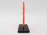 an orange sculpture on a black stand on a white surface