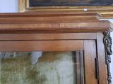 a wooden cabinet with a glass door and a painting on the wall behind it