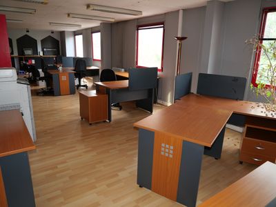 Il y a de nombreux bureaux et chaises dans ce bureau au sol en bois