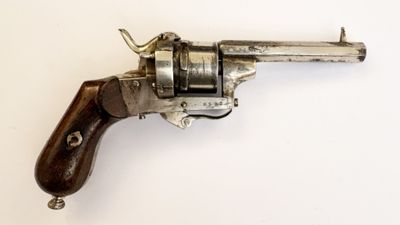un vieux revolver en argent avec une crosse en bois, posé sur une surface blanche