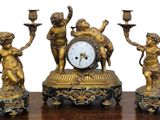 des figurines en laiton posées sur une table en bois, avec une horloge et des bougies