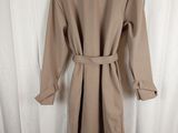 beige trench coat on a mannequin stand against a white curtain