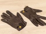 une paire de gants en cuir marron avec des boutons, posée sur une surface en bois